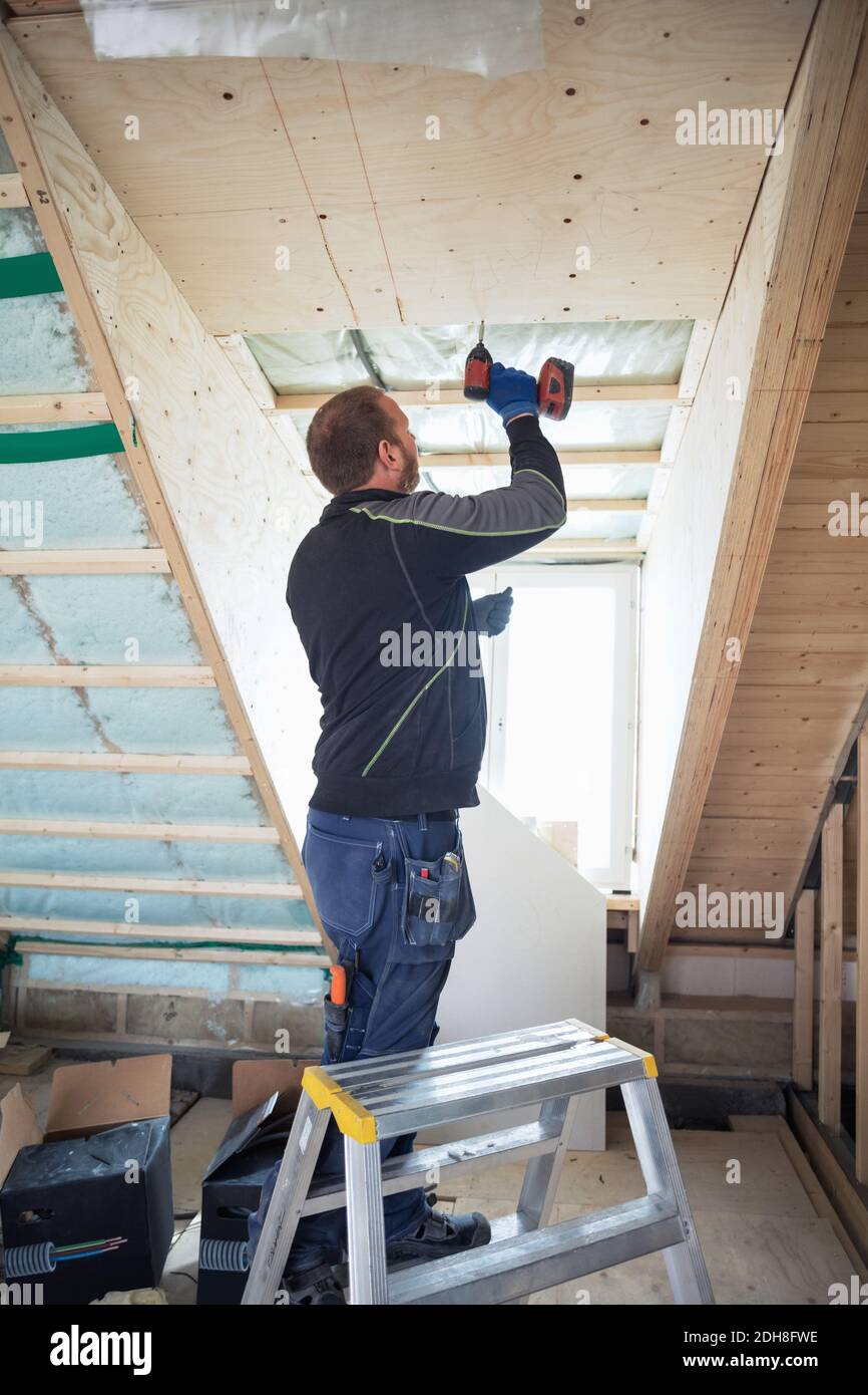 Homme forant des planches en bois sur la poutre de toit dans la maison Banque D'Images
