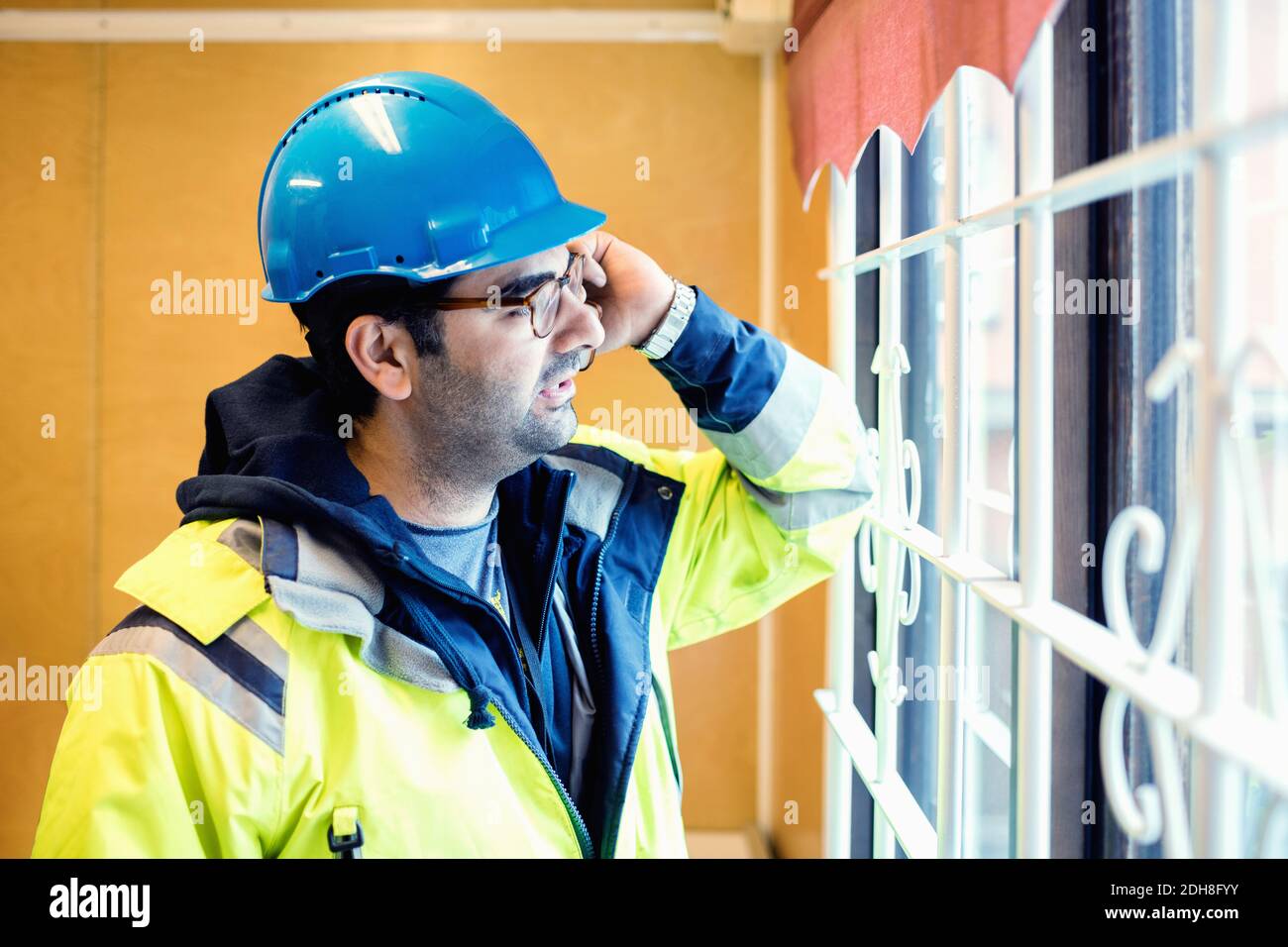 Ouvrier de la construction parlant au téléphone en se tenant près de la fenêtre industrie Banque D'Images