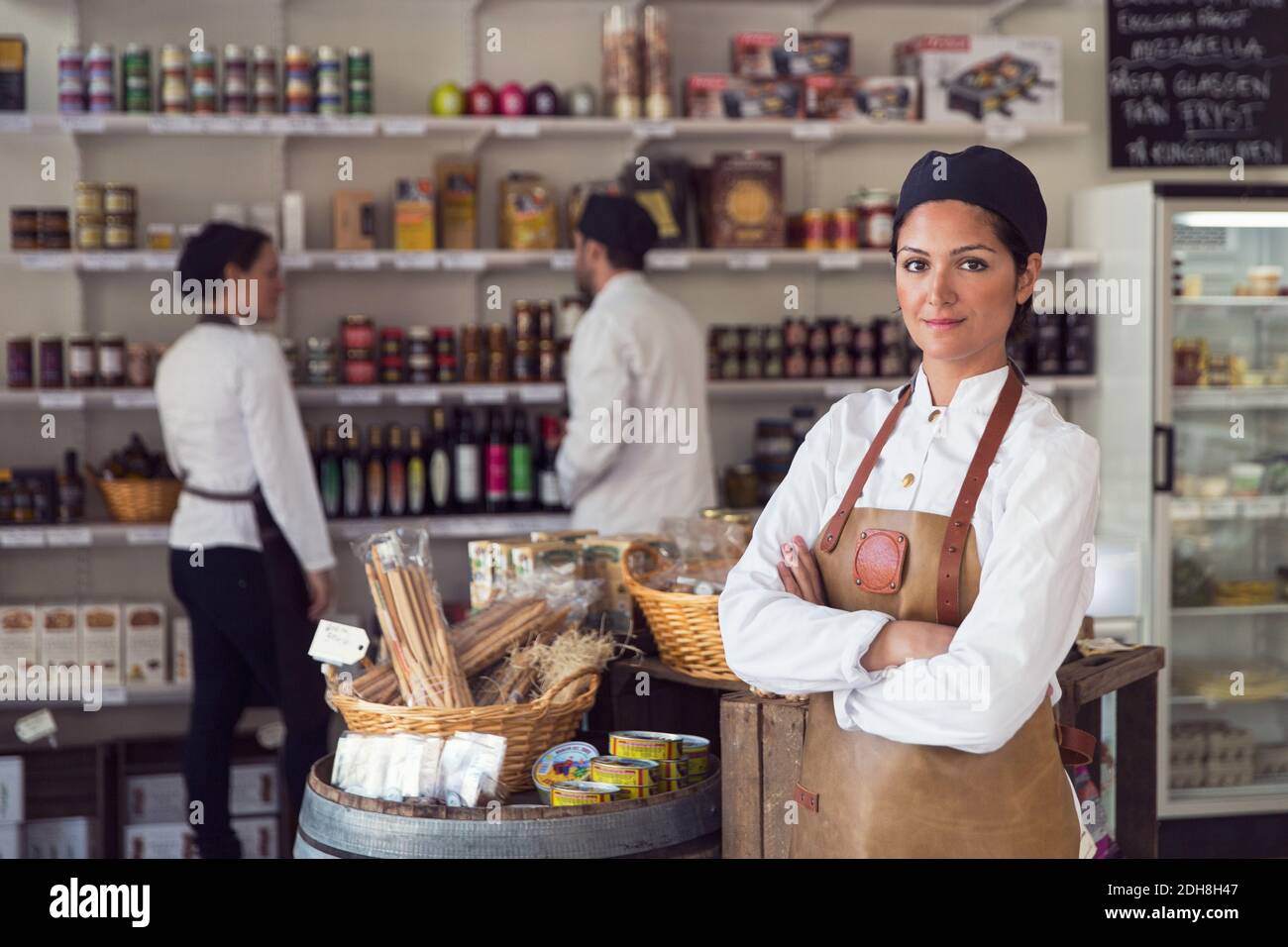 Portrait d'un propriétaire confiant debout bras croisés pendant que des collègues travaillent à l'épicerie Banque D'Images