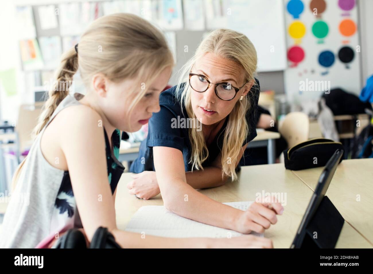 Enseignant aidant une écolière avec une tablette numérique dans la salle de classe Banque D'Images