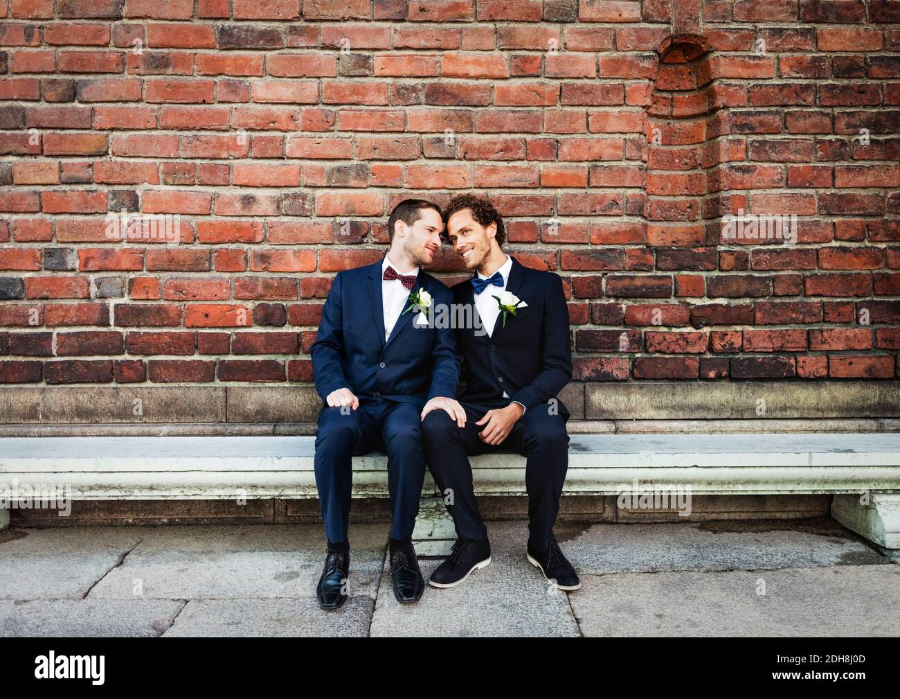 Couple gay nouvellement mariés assis sur un banc contre un mur de briques Banque D'Images