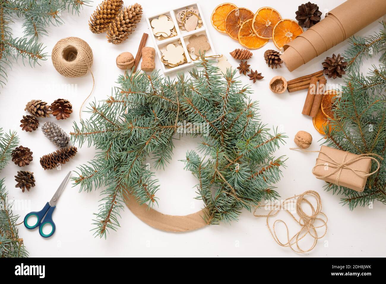 Processus étape par étape de fabrication de la couronne d'arbres de Noël à la maison à partir de branches d'épinette, d'oranges et de jouets écologiques en bois en 2021. Fond blanc Banque D'Images