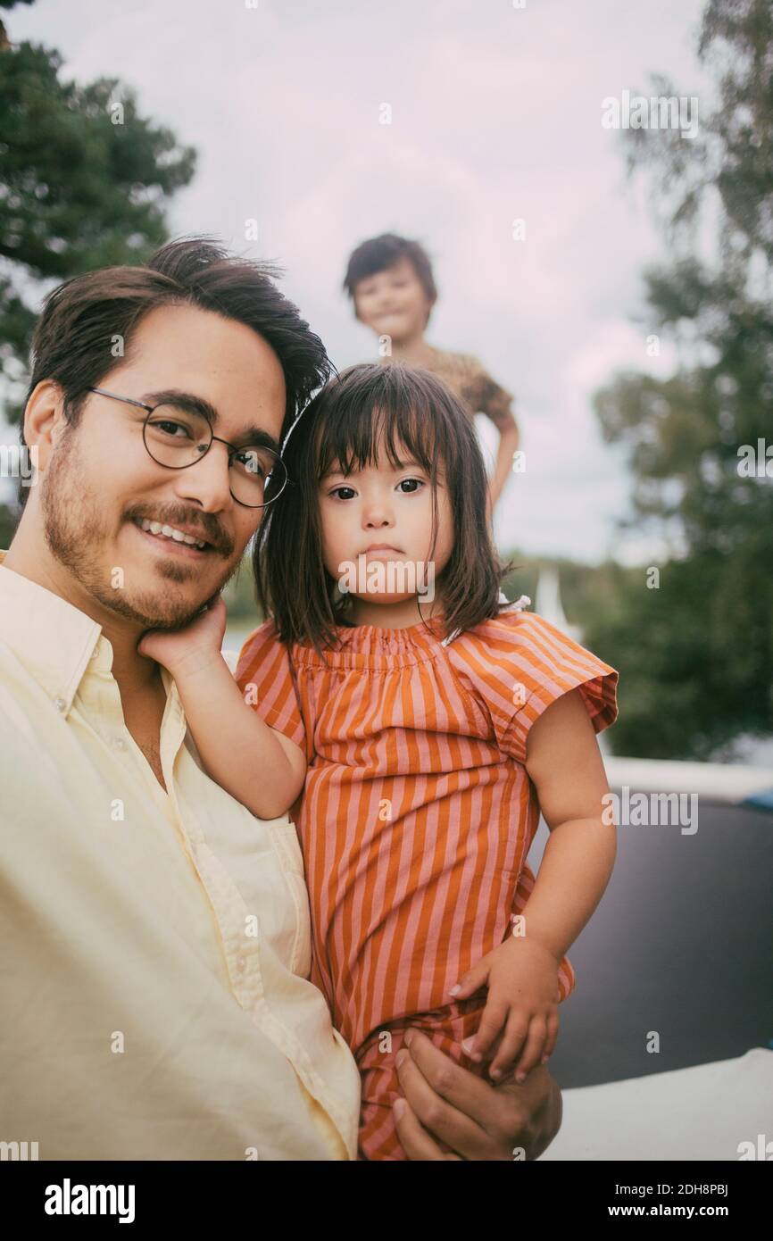 Portrait de père souriant transportant le syndrome de fille debout contre fille sur trampoline pendant l'été Banque D'Images