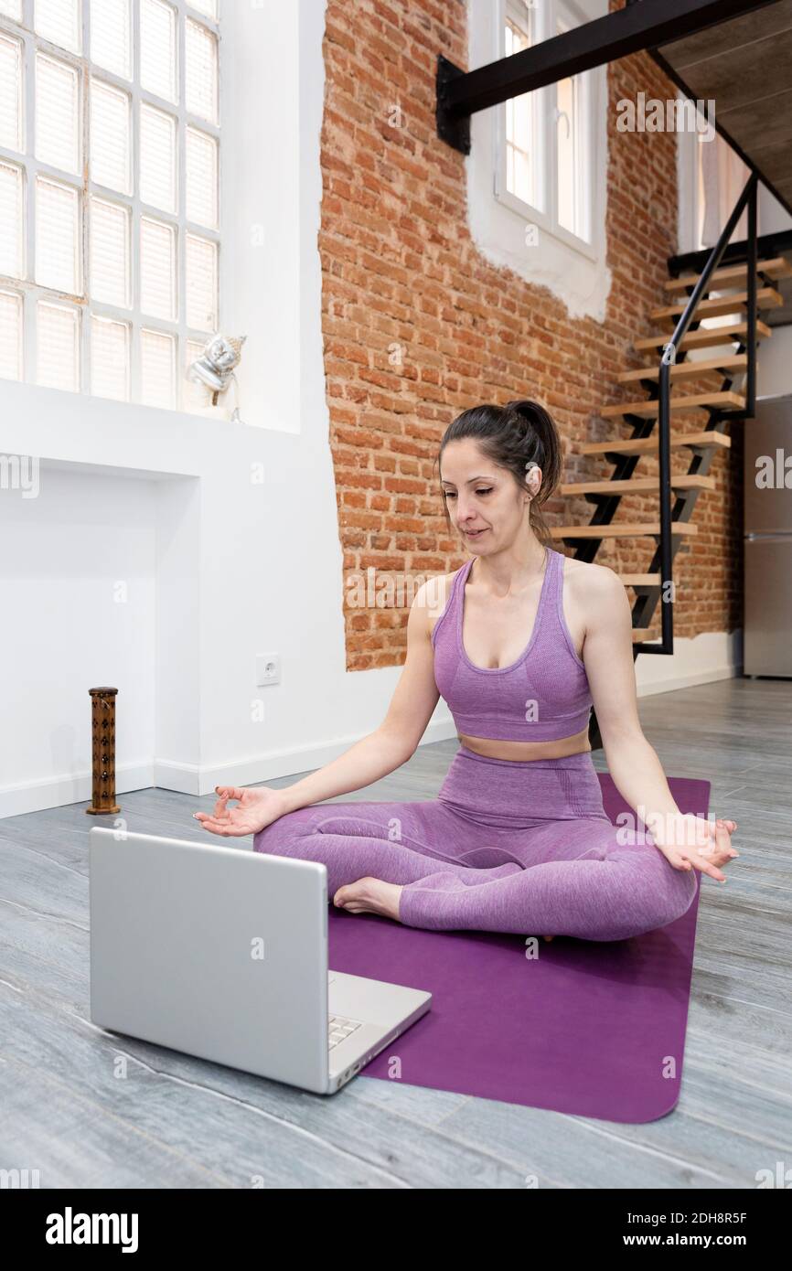 Jeune femme pratiquant la posture de méditation de yoga devant son ordinateur portable. Concept de cours en ligne à partir de la maison. Banque D'Images
