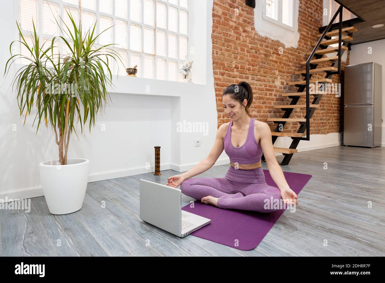 Une jeune fille athlétique qui fait de la posture de méditation de yoga devant son ordinateur portable à la maison. Concept des cours en ligne. Banque D'Images