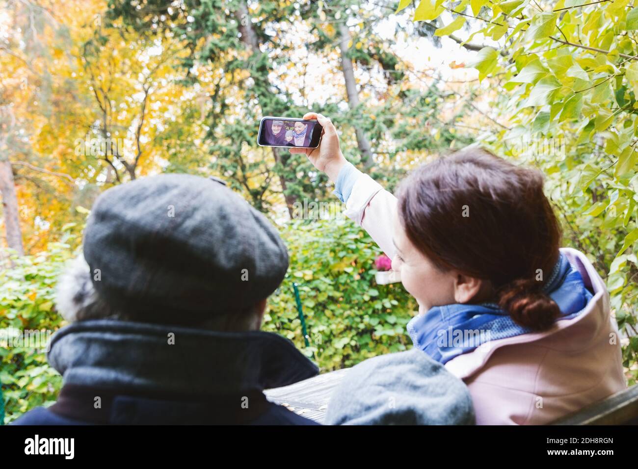 Une femme qui prend son selfie avec son smartphone et sa famille au parc en automne Banque D'Images