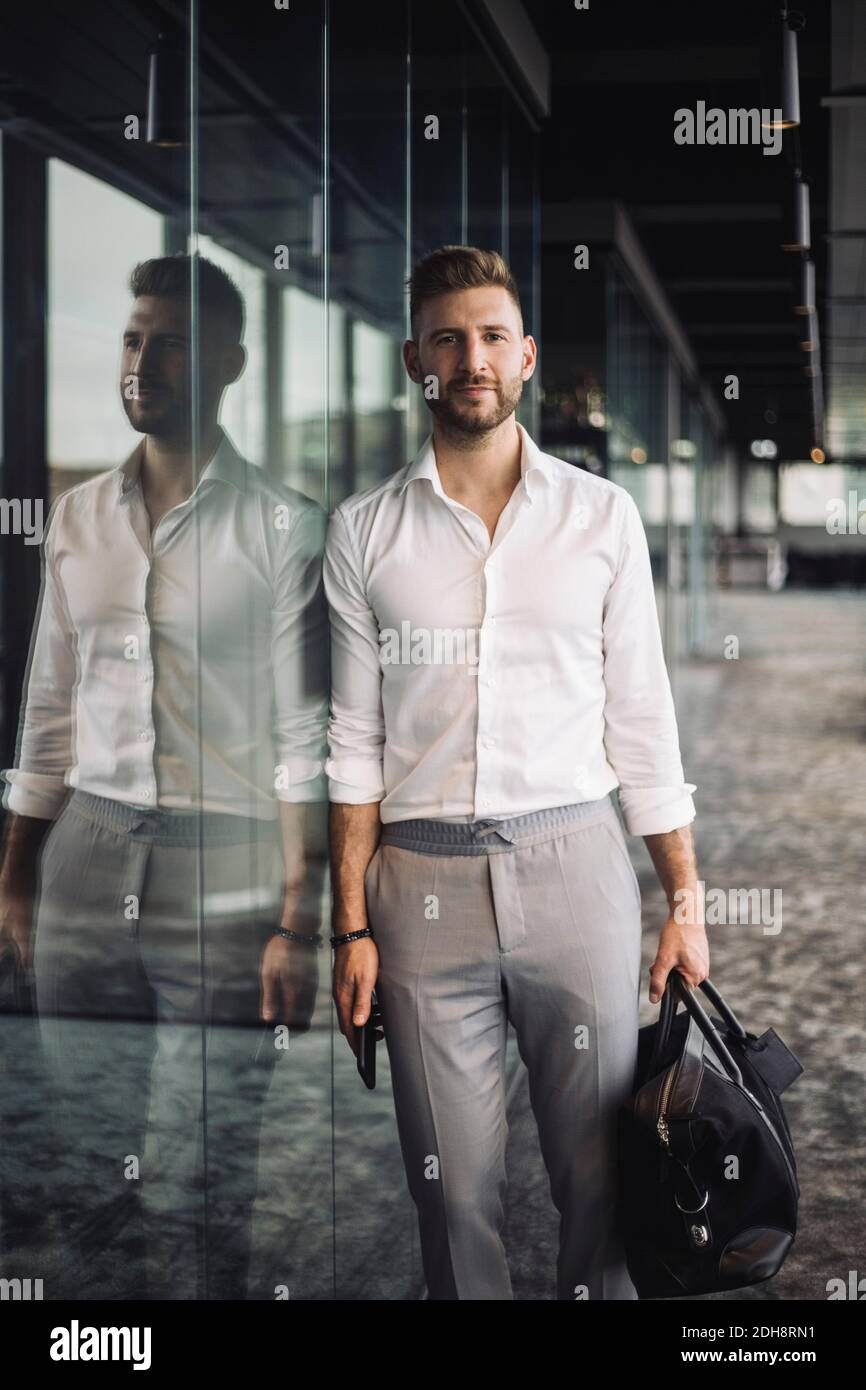 Portrait d'entrepreneur masculin avec sac incliné sur fenêtre en verre au bureau Banque D'Images