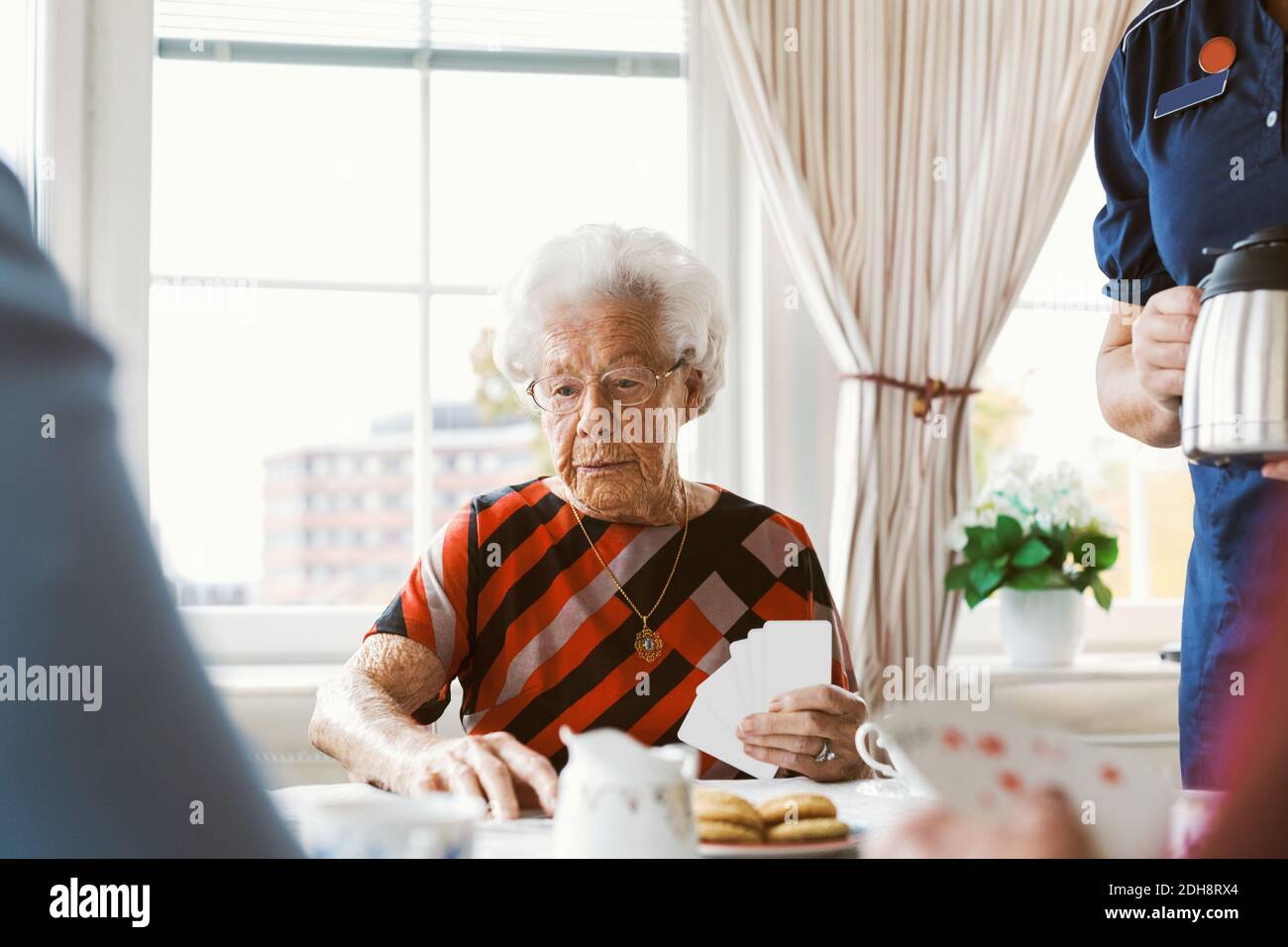 Femme âgée jouant des cartes avec la famille tout en tenant le café par un gardien pot à la maison Banque D'Images