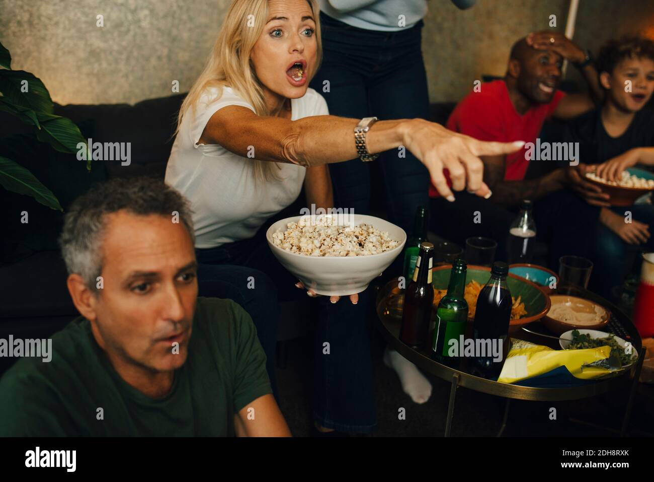 Femme avec la bouche ouverte gestant par la famille tout en mangeant du pop-corn pendant un événement sportif Banque D'Images