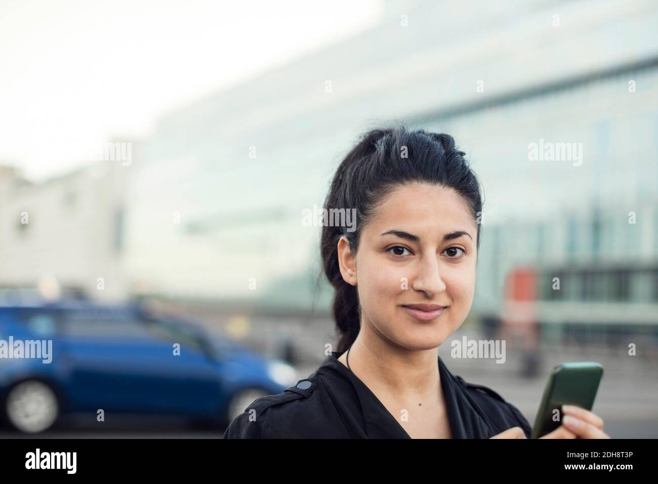 Portrait d'une femme confiante avec un téléphone portable contre un bâtiment Banque D'Images