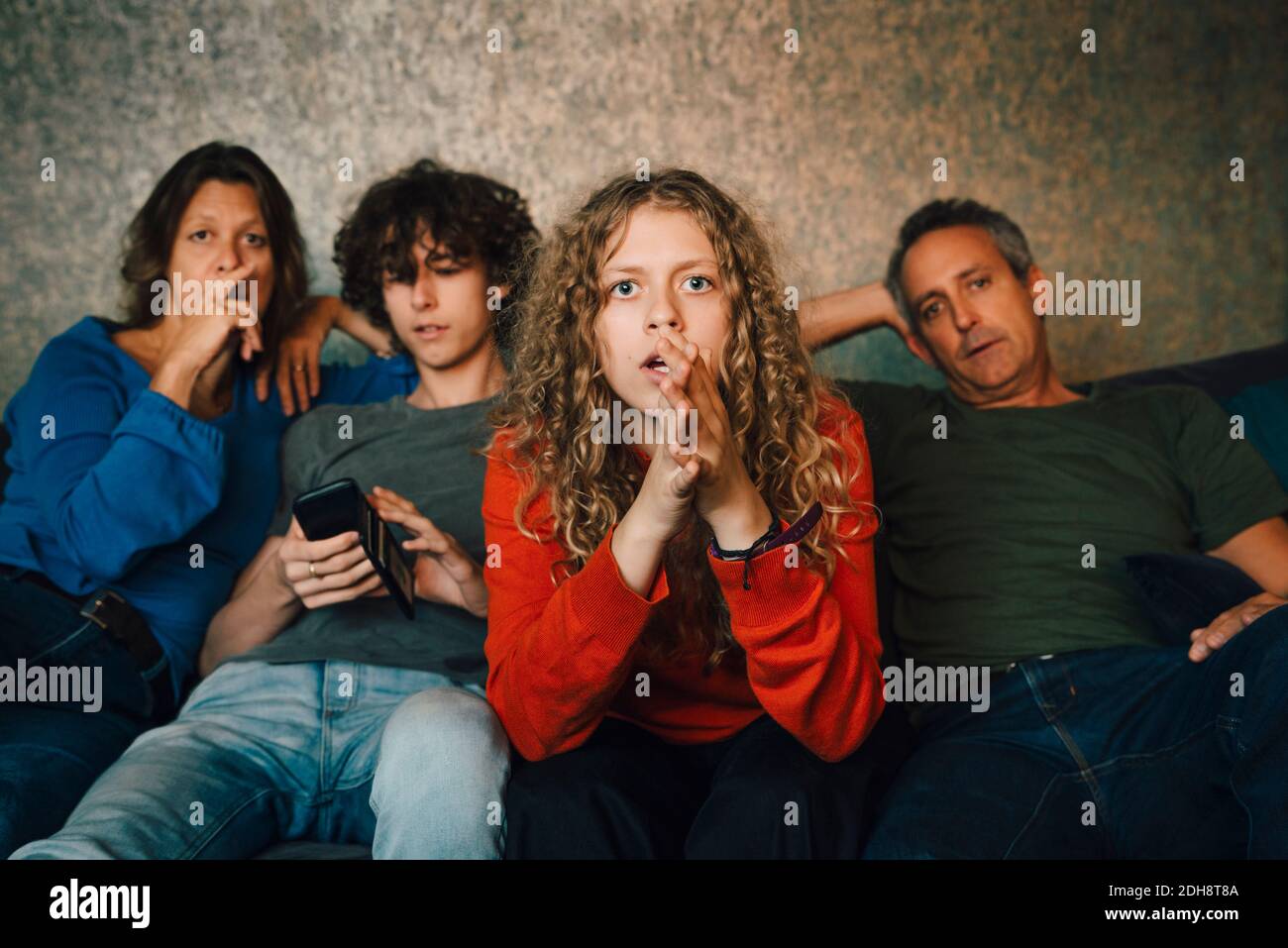 Fille priant tout en regardant le sport avec la famille à la maison Banque D'Images