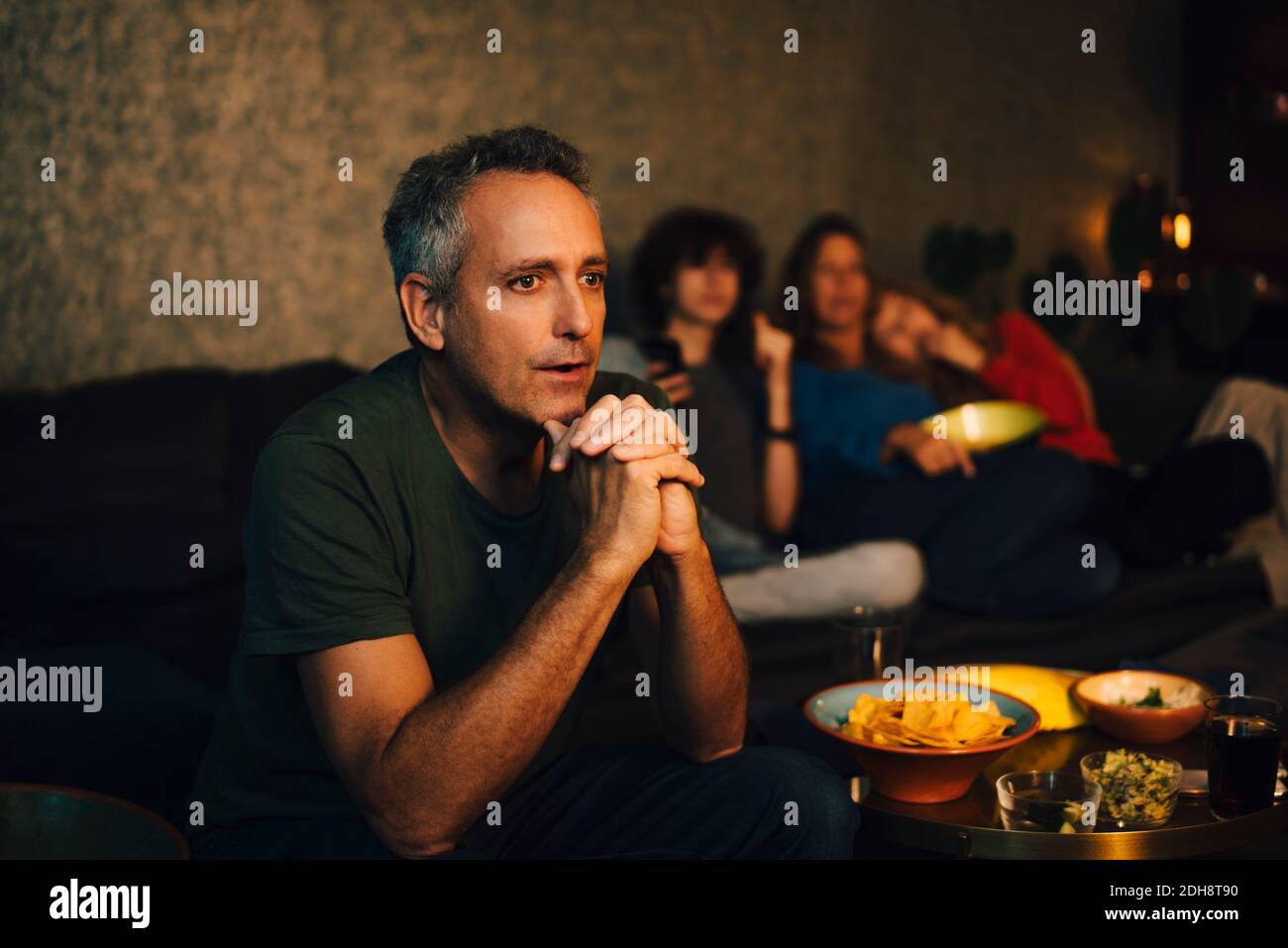 Homme plein d'espoir priant tout en regardant le sport dans le salon à nuit Banque D'Images