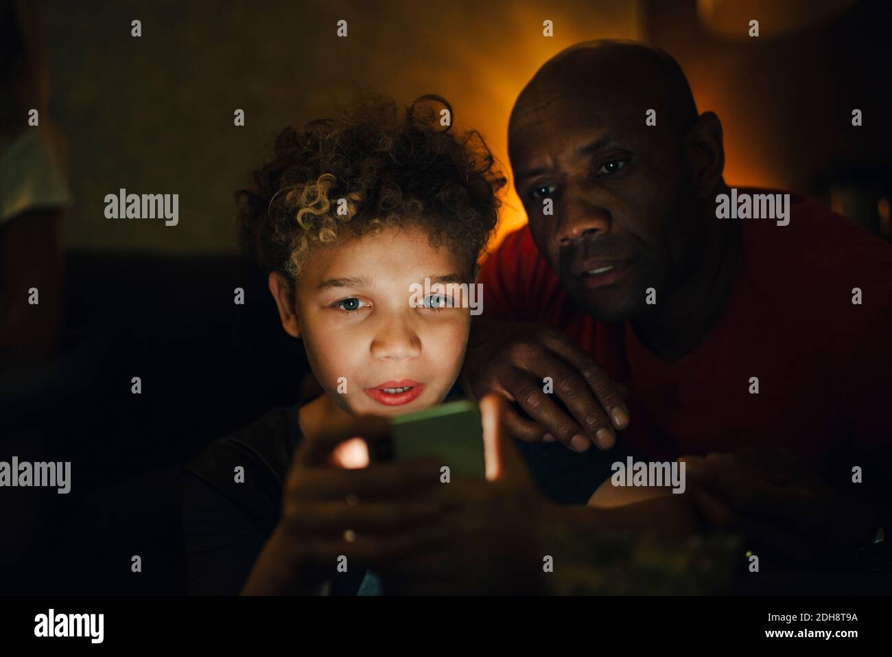 Garçon utilisant un smartphone par père dans le salon à nuit Banque D'Images