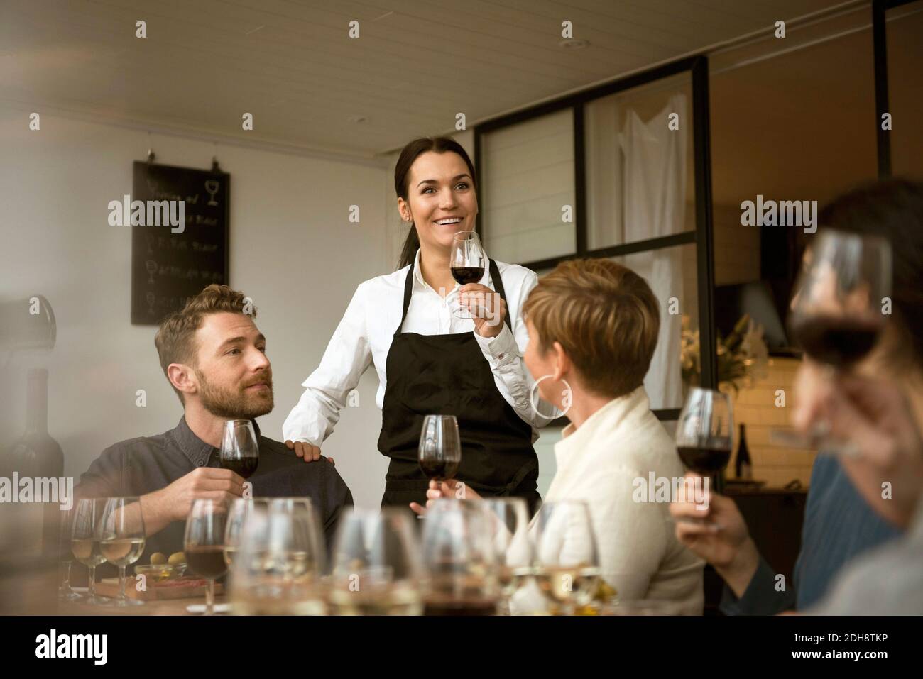 Femme souriante portant un tablier tenant des lunettes de vin avec des gens d'affaires à tableau Banque D'Images