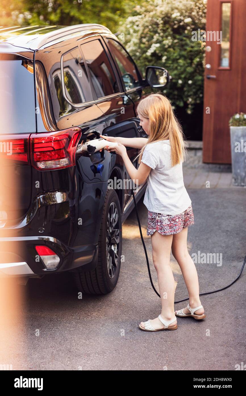 Une fille blonde charge une voiture électrique noire dans la cour arrière Banque D'Images