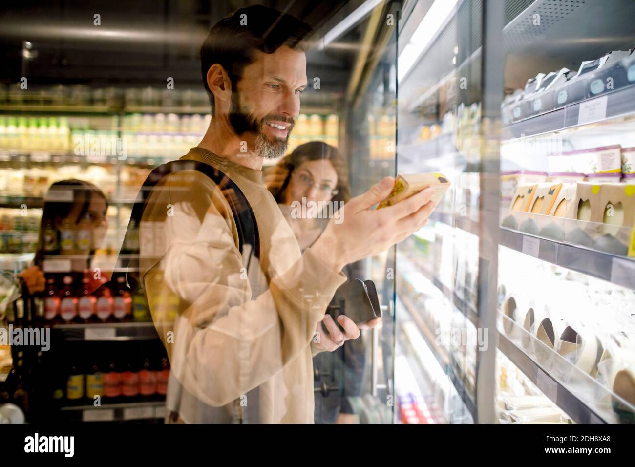 Un client souriant lisant des ingrédients tout en faisant du shopping en famille dans un supermarché Banque D'Images