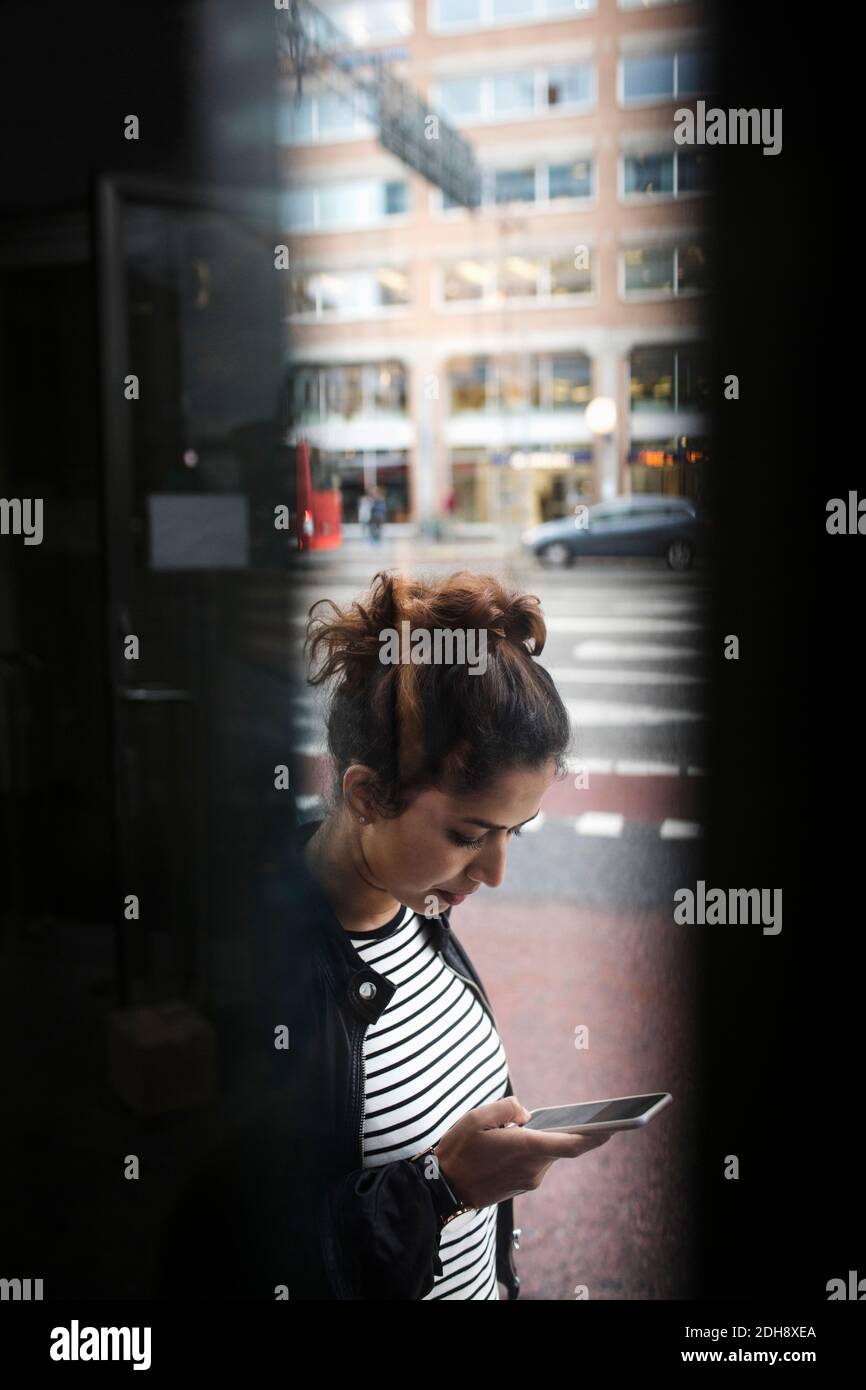 Femme utilisant le téléphone par la rue de ville vu par la fenêtre Banque D'Images