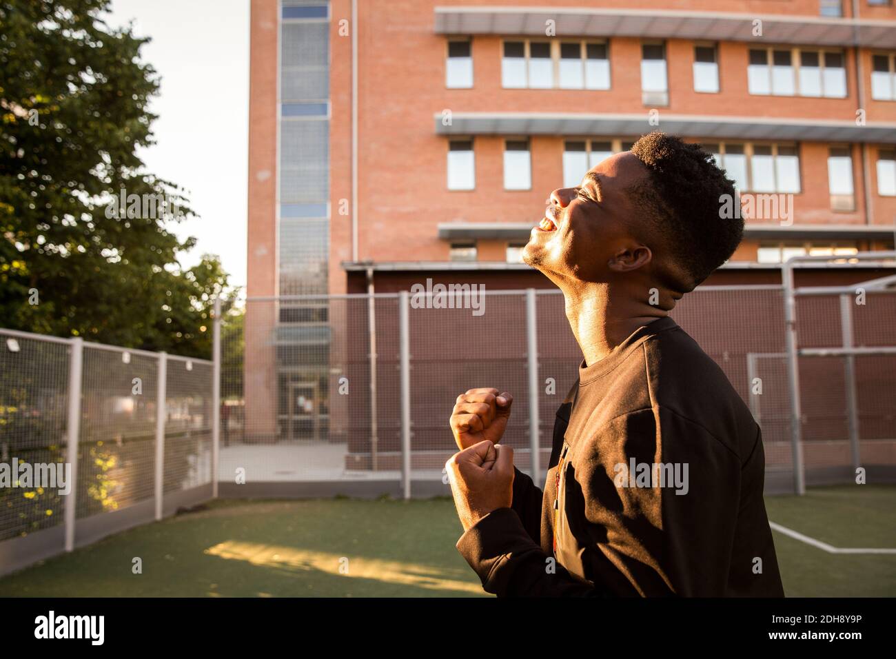 Vue latérale d'un jeune homme souriant qui applaudisse les yeux fermés sur le terrain de sport Banque D'Images