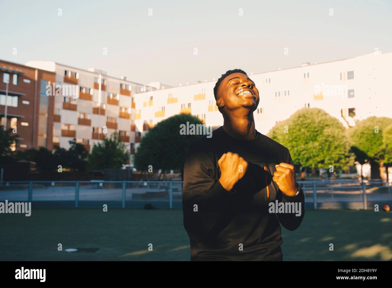 Jeune homme souriant qui applaudisse avec les yeux fermés dans le champ sportif Banque D'Images