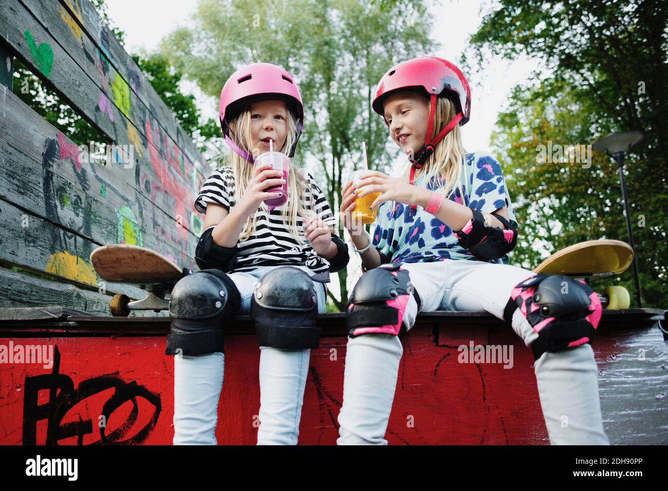 Des amis souriants se régarent d'un verre tout en étant assis sur le bord du skateboard rampe Banque D'Images