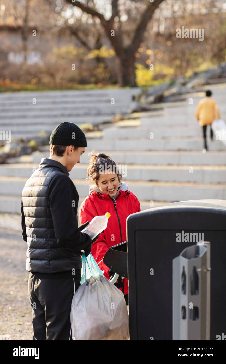 Souriant, des volontaires hommes et femmes jettent des déchets plastiques dans les ordures can Banque D'Images