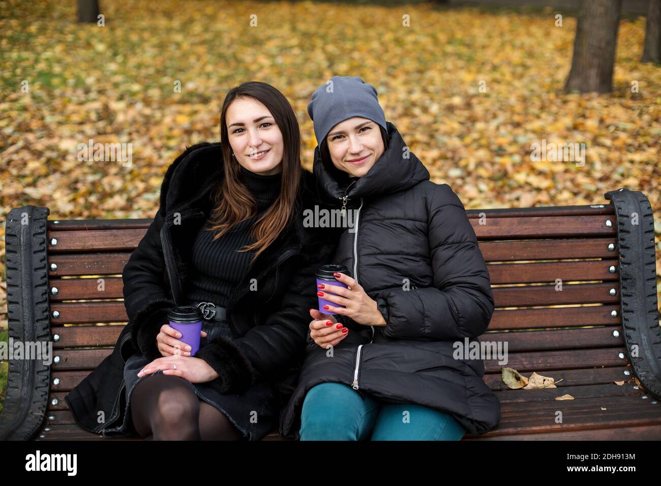 Deux filles dans le parc parlent sur un banc avec un téléphone et un verre. Banque D'Images