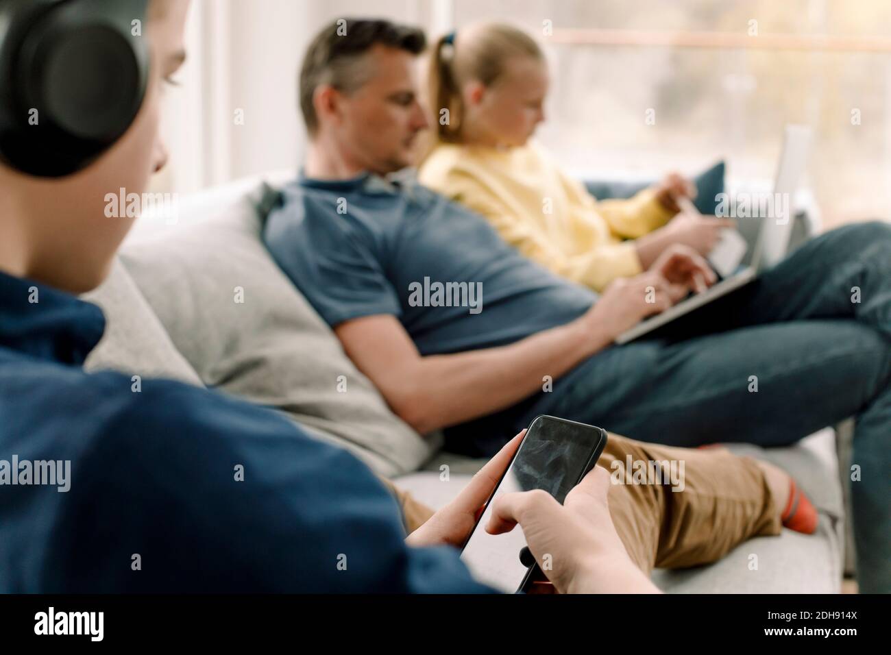 Adolescent utilisant un téléphone intelligent tout en étant assis sur un canapé avec la famille Banque D'Images