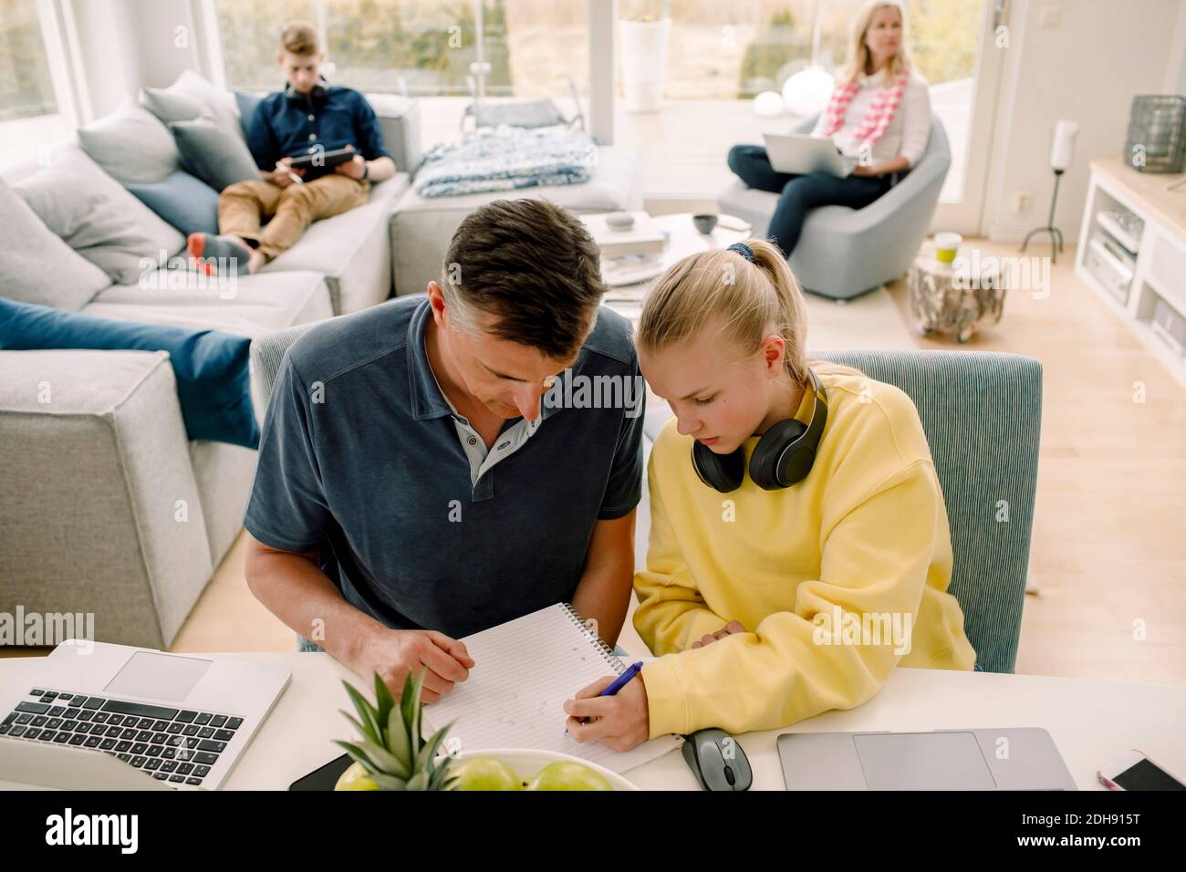 Vue en grand angle de la fille enseignante du père pendant qu'elle est assise table dans la salle de séjour Banque D'Images