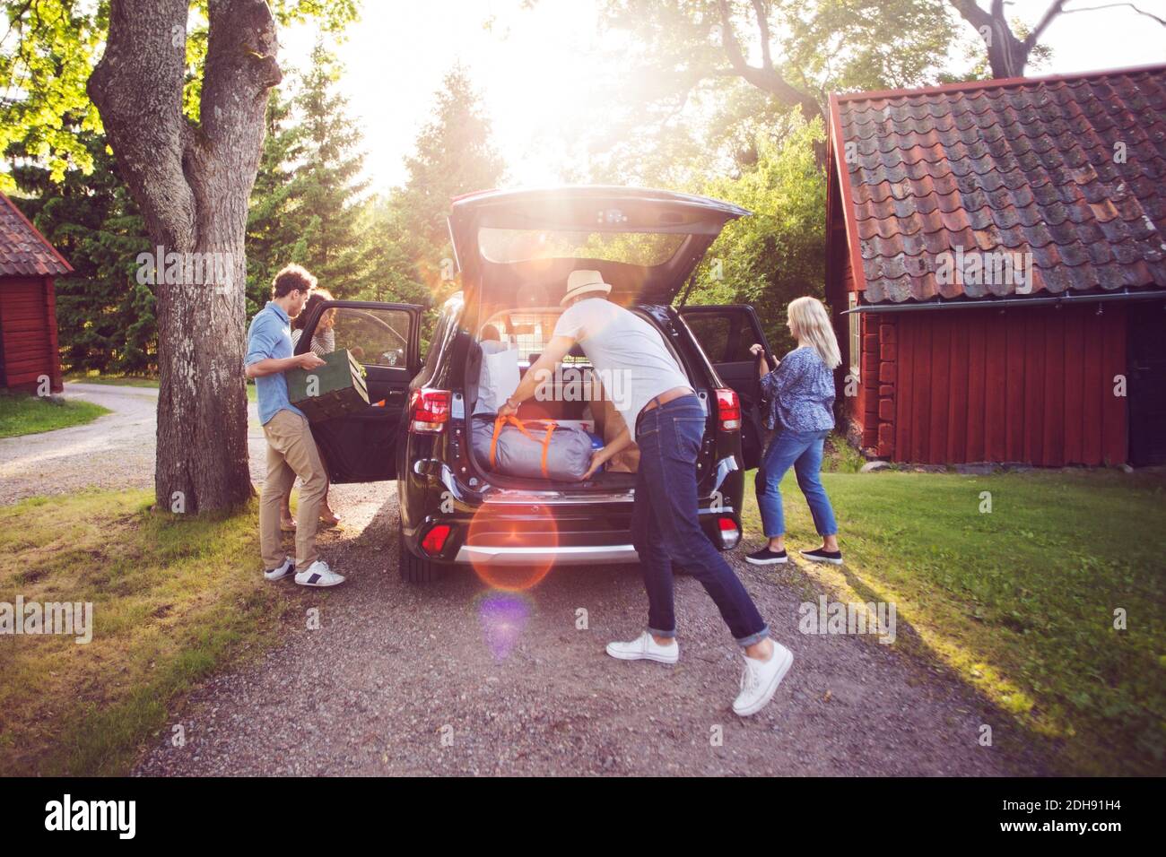 Des amis qui chargent leurs bagages en voiture sur la route par beau temps Banque D'Images