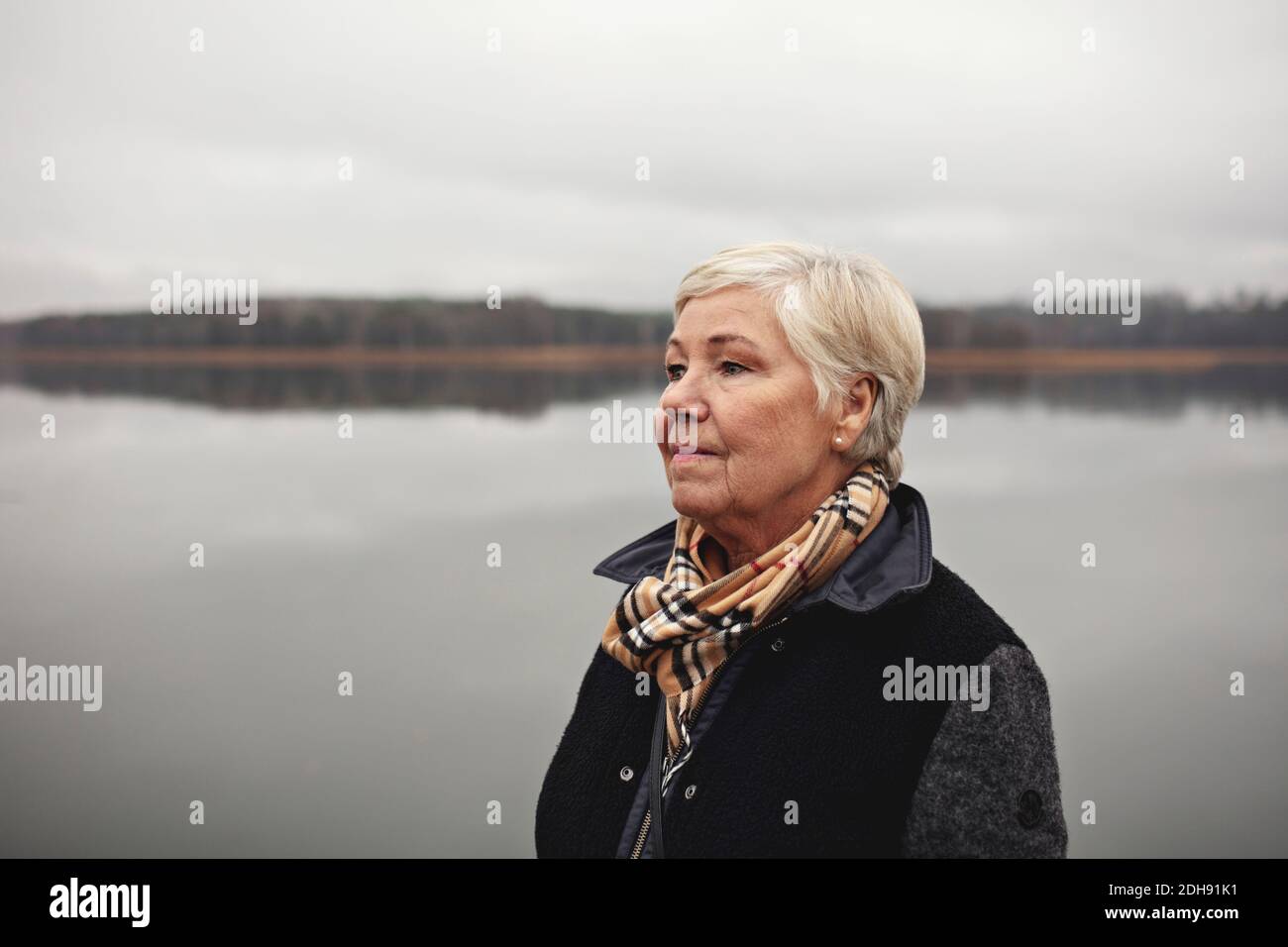 Femme ridée souriante regardant loin du lac contre le ciel clair Banque D'Images