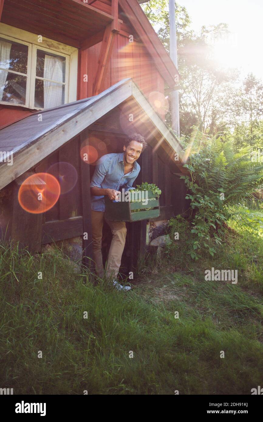 Homme souriant portant une caisse tout en sortant du cottage jour ensoleillé Banque D'Images