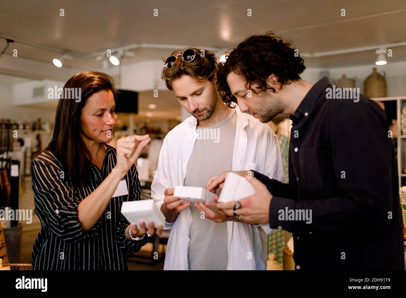 Une vendeuse montrant une boîte de parfum à des amis masculins en magasin Banque D'Images