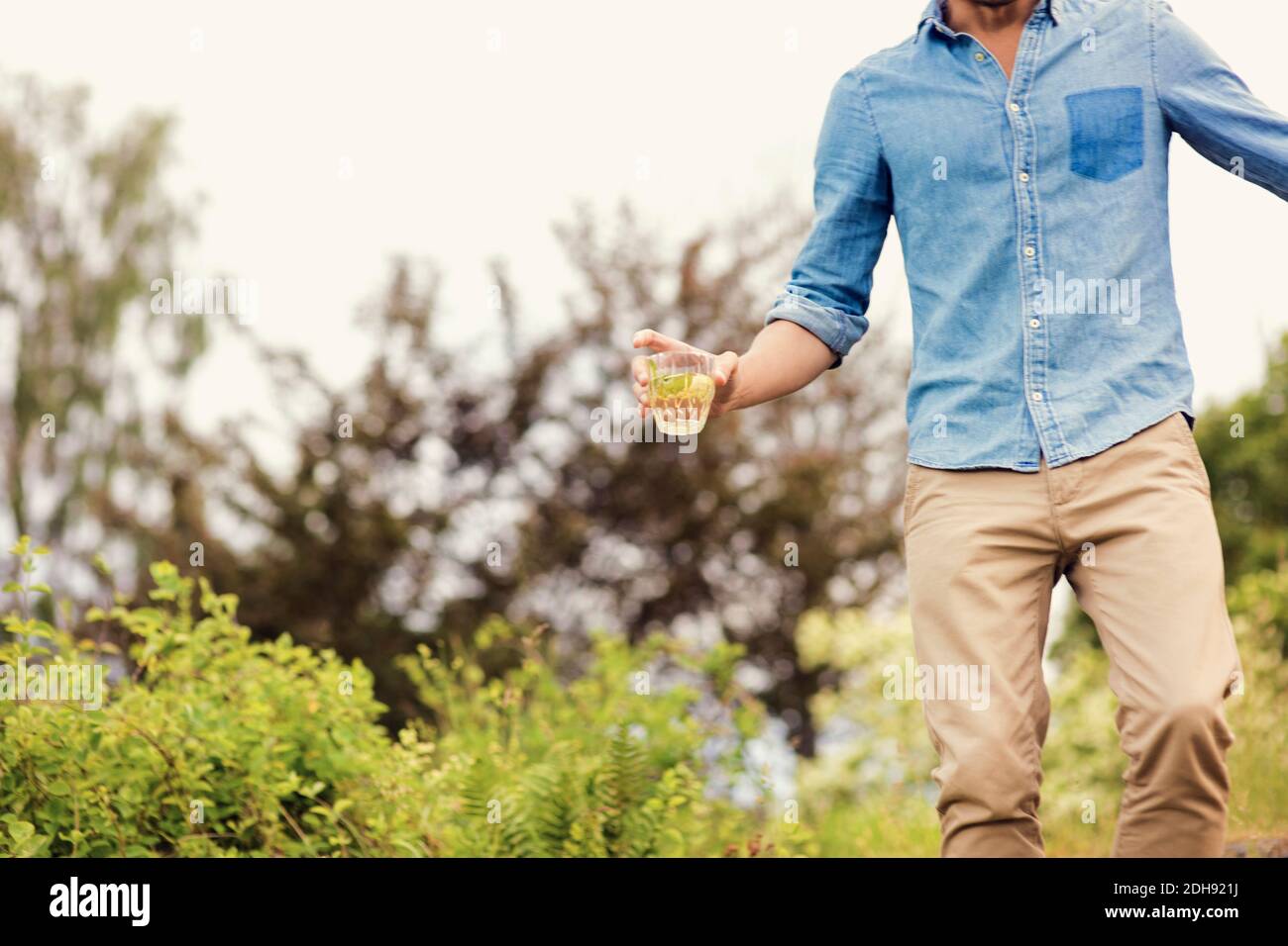 Section médiane de l'homme tenant la boisson tout en se tenant contre les plantes Banque D'Images