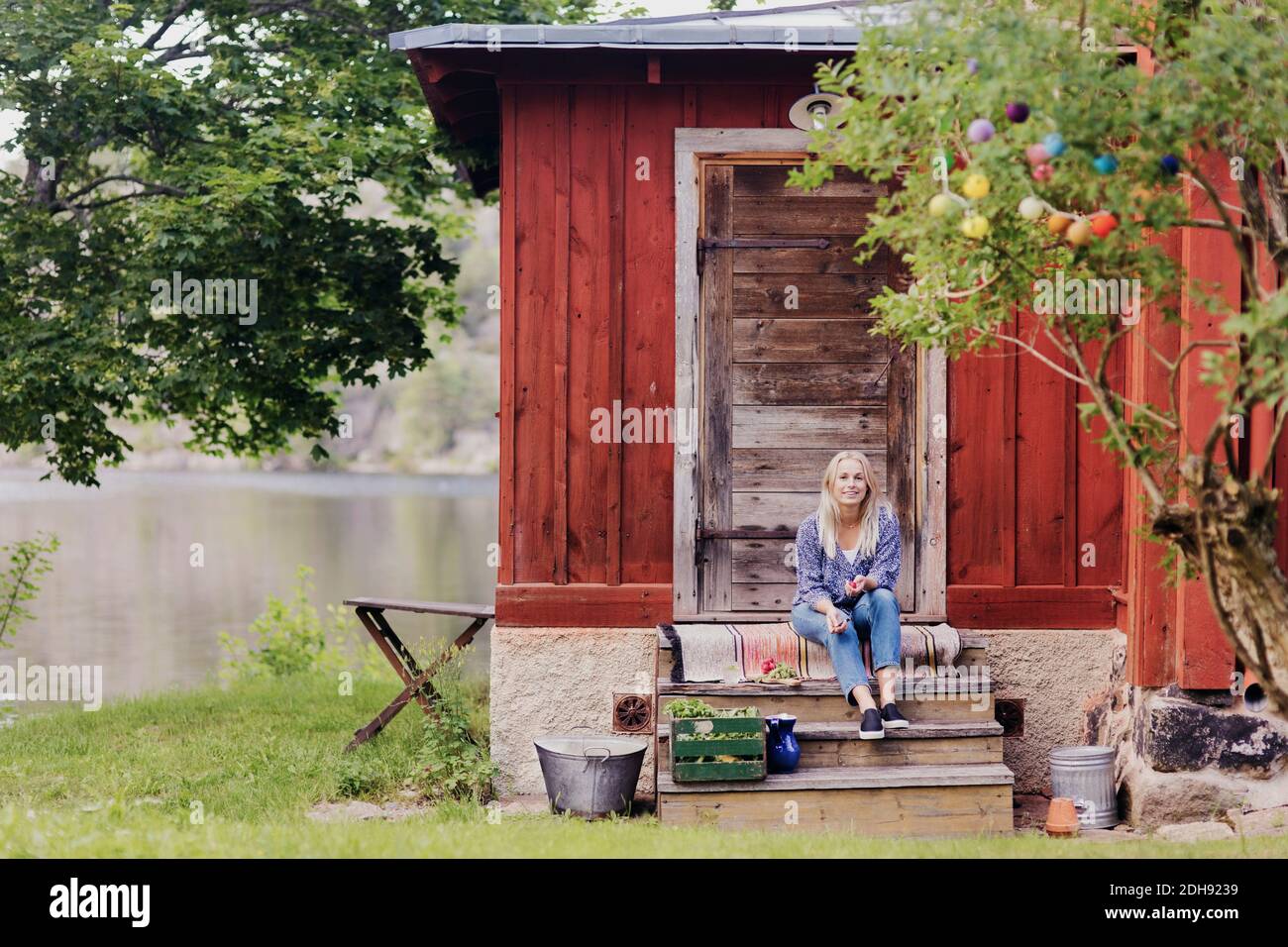 Femme souriante avec des légumes biologiques assis à l'extérieur du cottage en bois Banque D'Images