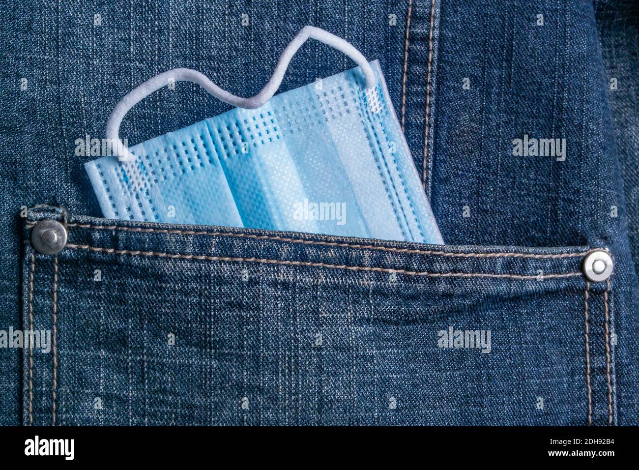 un masque antiviral de protection médicale dépasse de la poche de une veste en denim Banque D'Images