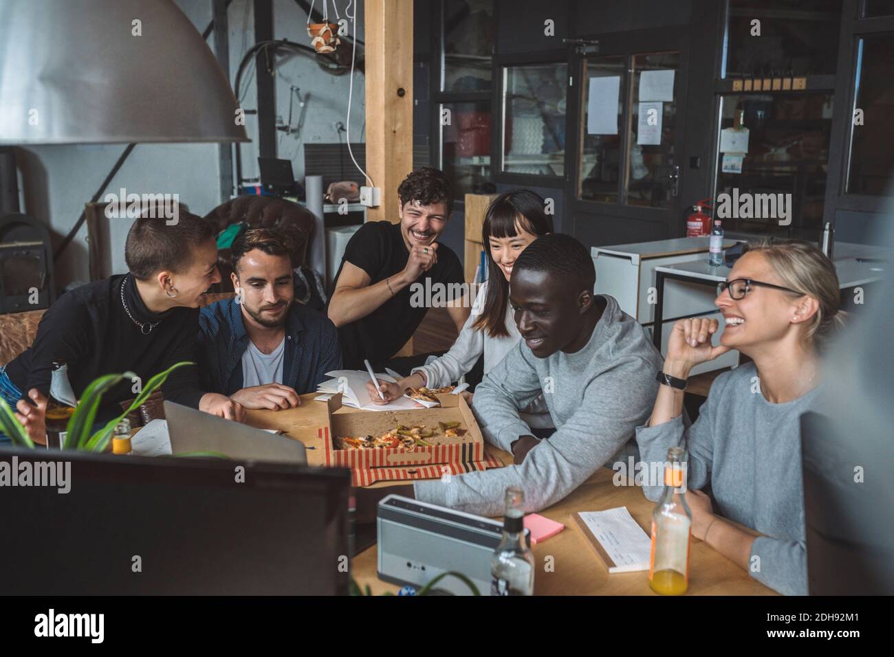 Des collègues souriants mangent de la pizza tout en travaillant sur le lieu de travail Banque D'Images