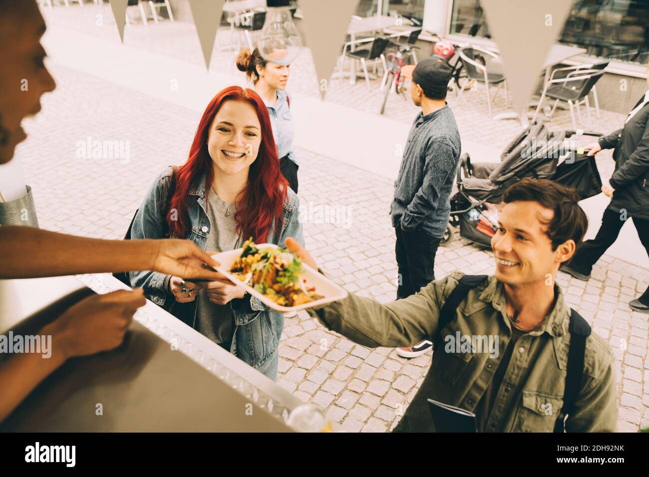 Femme assistant donnant une assiette à un client souriant en ville Banque D'Images