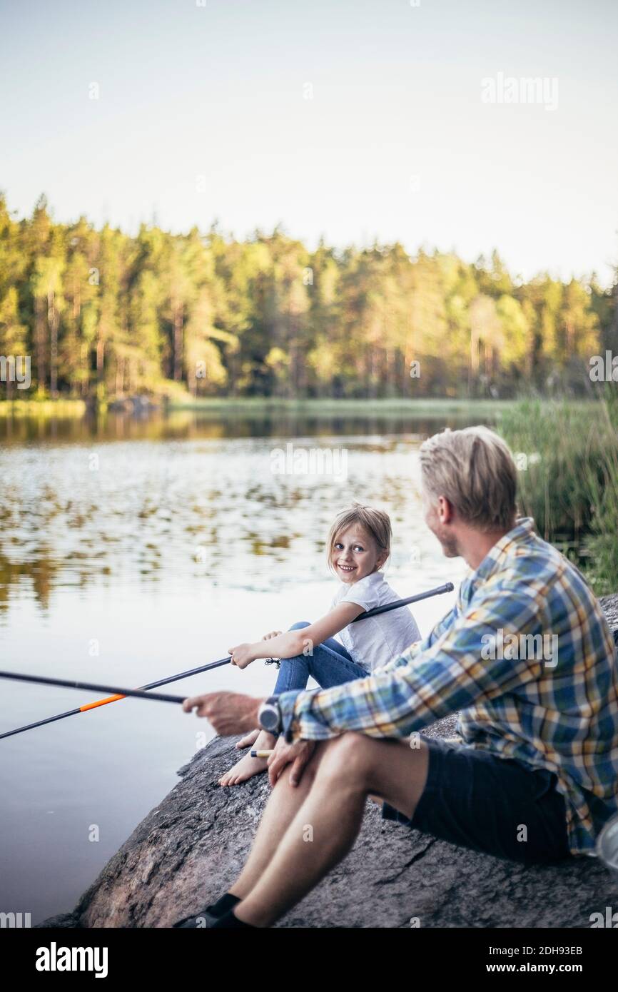 Fille souriante regardant le père tout en pêchant au lac Banque D'Images
