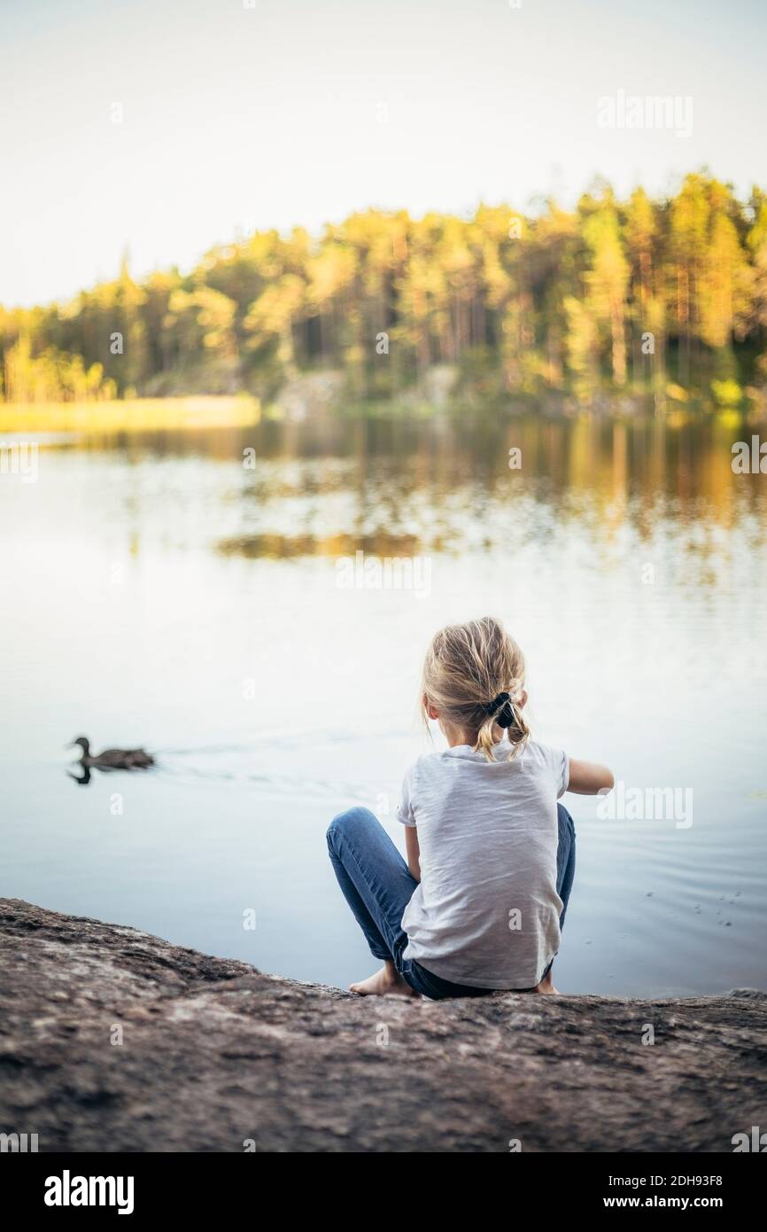 Vue arrière d'une fille assise sur un rocher au lac Banque D'Images