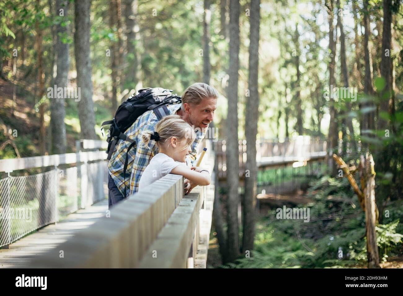Père souriant avec sac à dos parlant à la fille sur la passerelle à l'intérieur forêt Banque D'Images