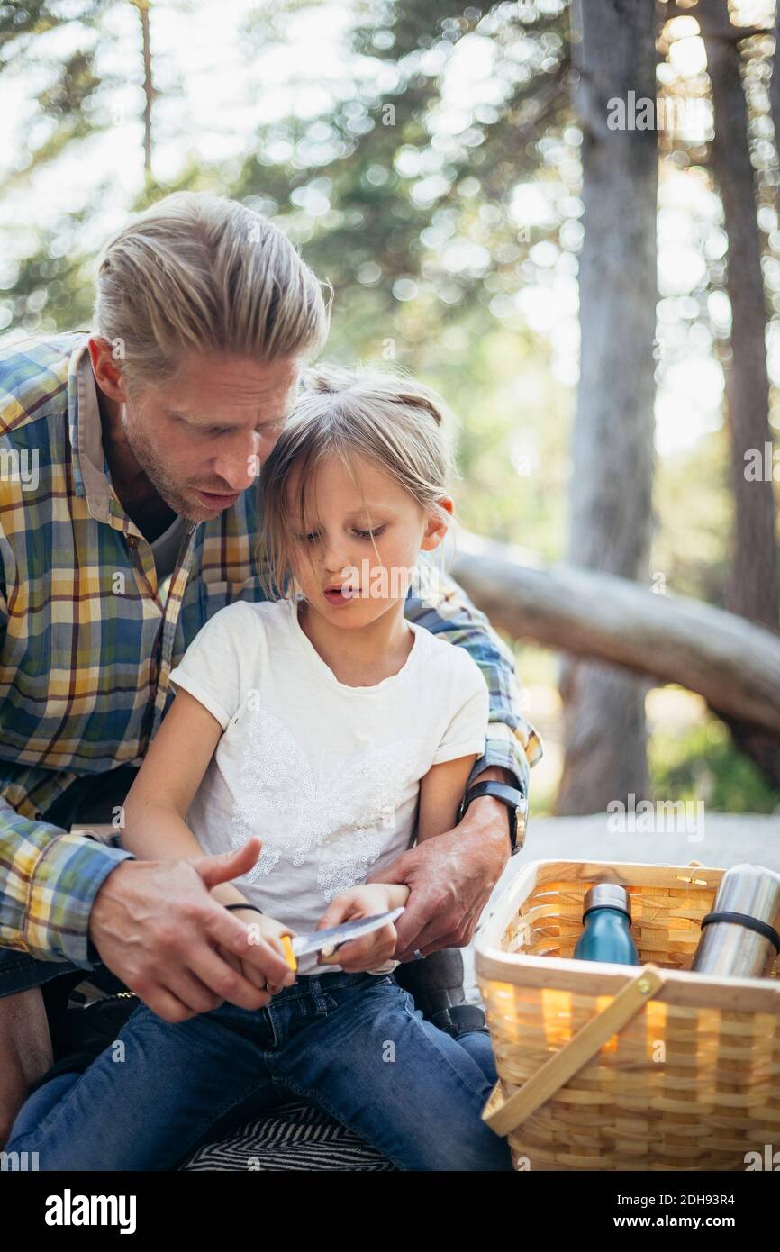 Père aidant fille à couper bâton avec couteau dans la forêt Banque D'Images