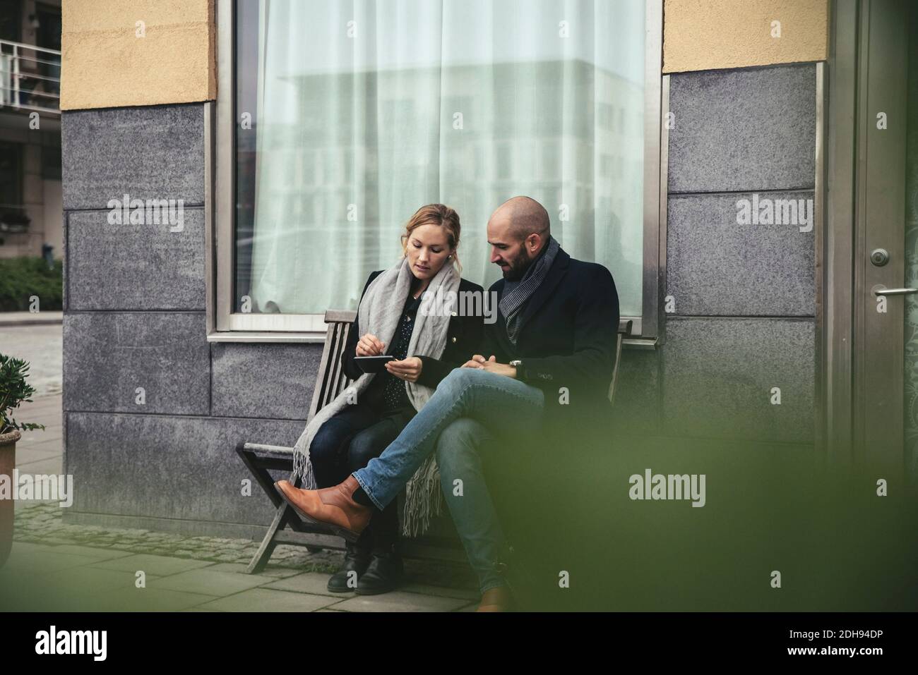 Nombre total de personnes de taille moyenne utilisant un smartphone sur le banc contre le bâtiment Banque D'Images