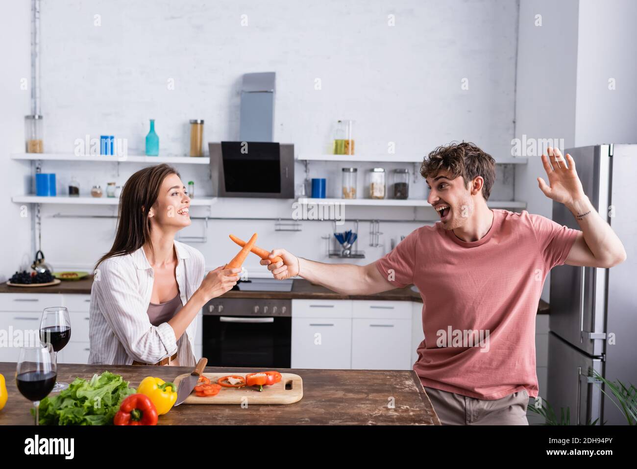 Couple gai luttant avec des carottes près des légumes et du vin Banque D'Images