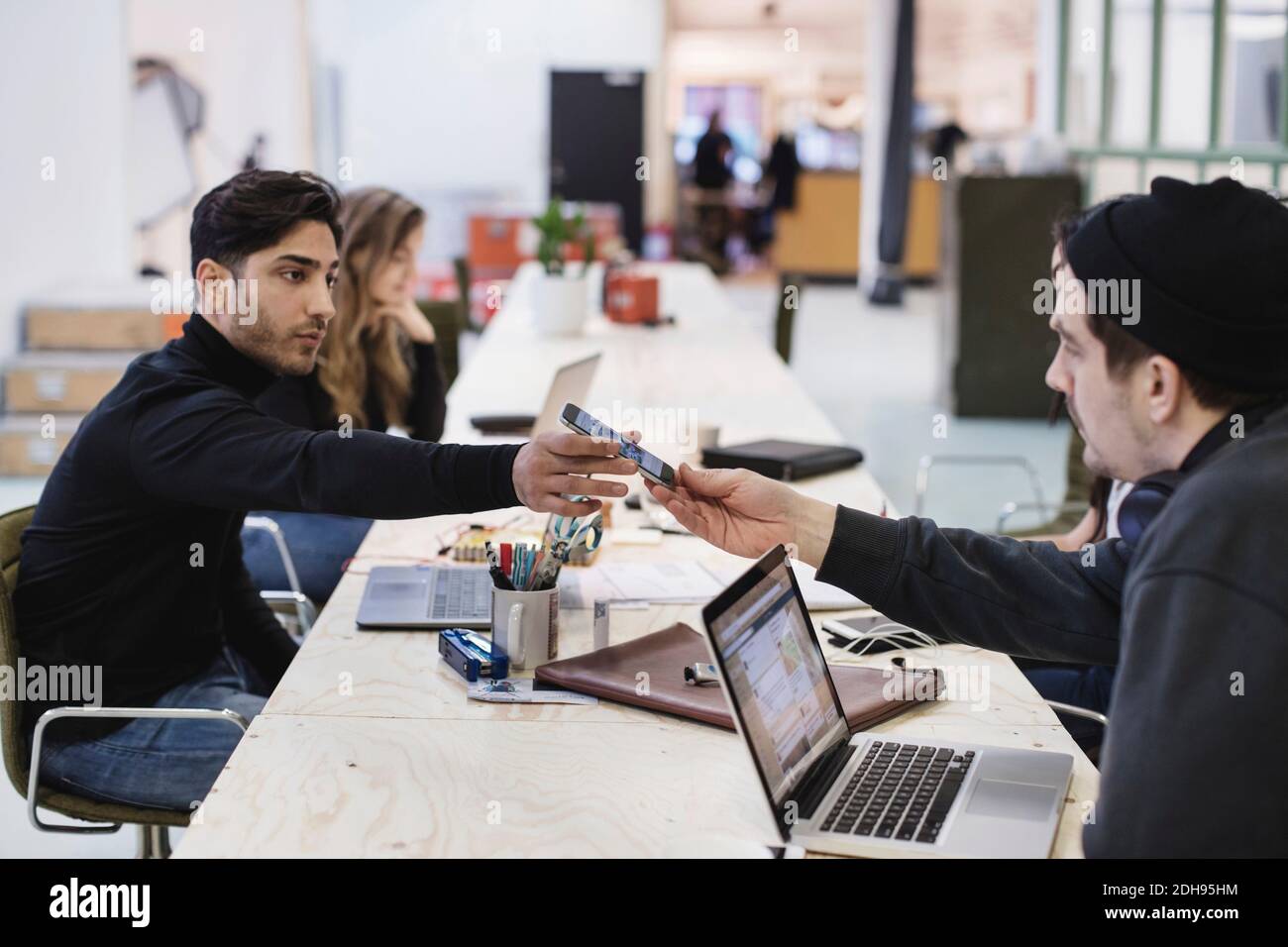 Vue latérale d'un jeune homme qui donne un smartphone à un collègue au bureau Banque D'Images