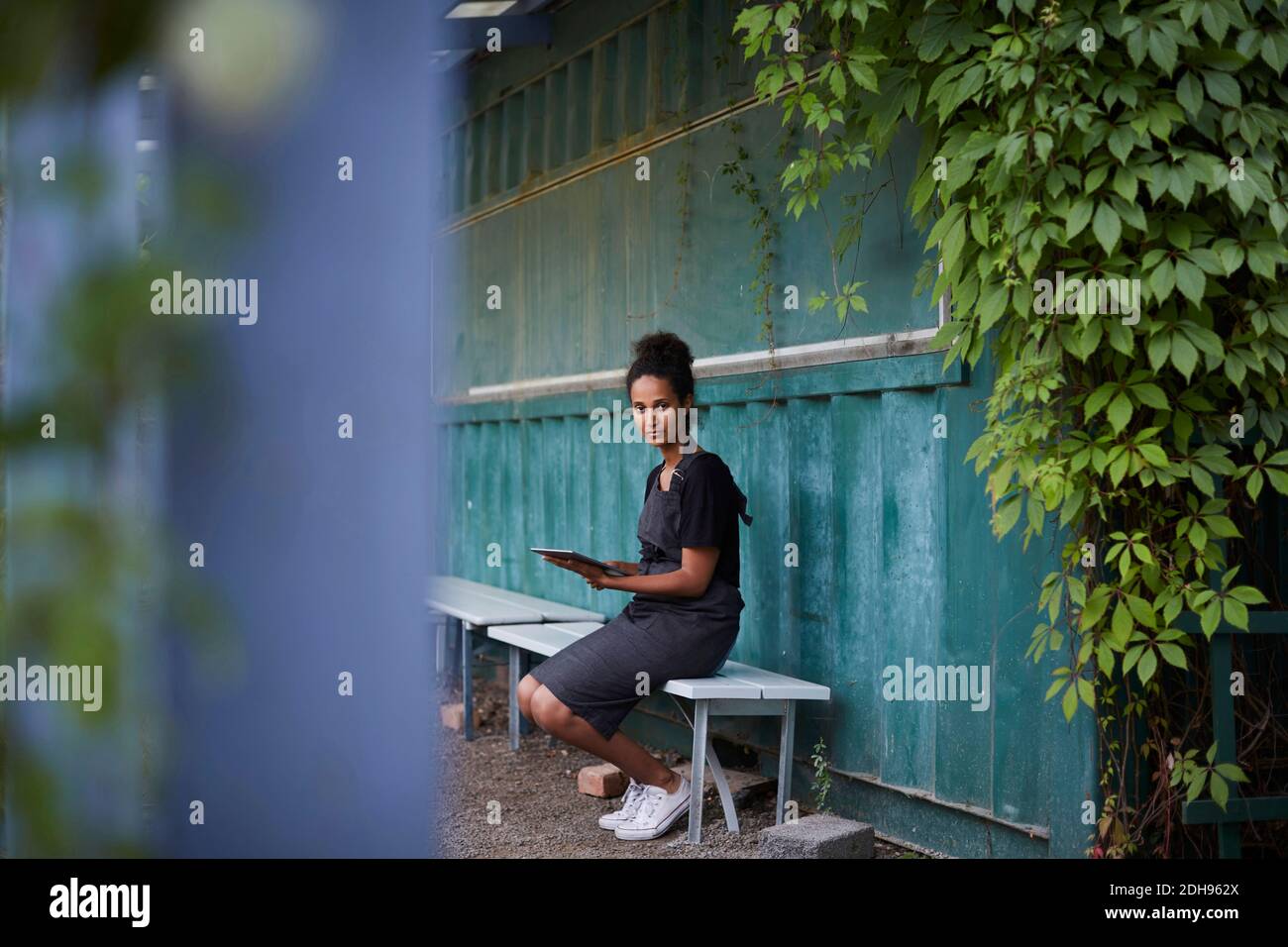 Portrait d'une femme jardinière tenant une tablette numérique assise sur banc Banque D'Images