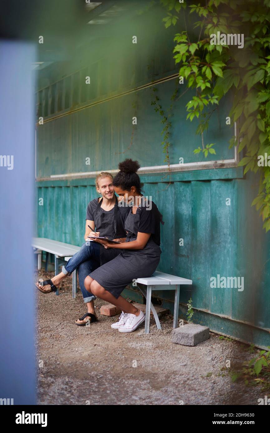 Pleine longueur de jardiniers avec tablette numérique assis sur le banc dans la cour Banque D'Images