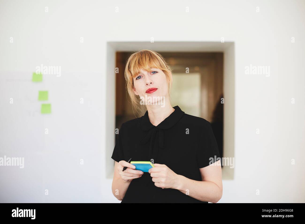 Portrait d'une femme d'affaires confiante tenant un bloc-notes collant au bureau Banque D'Images