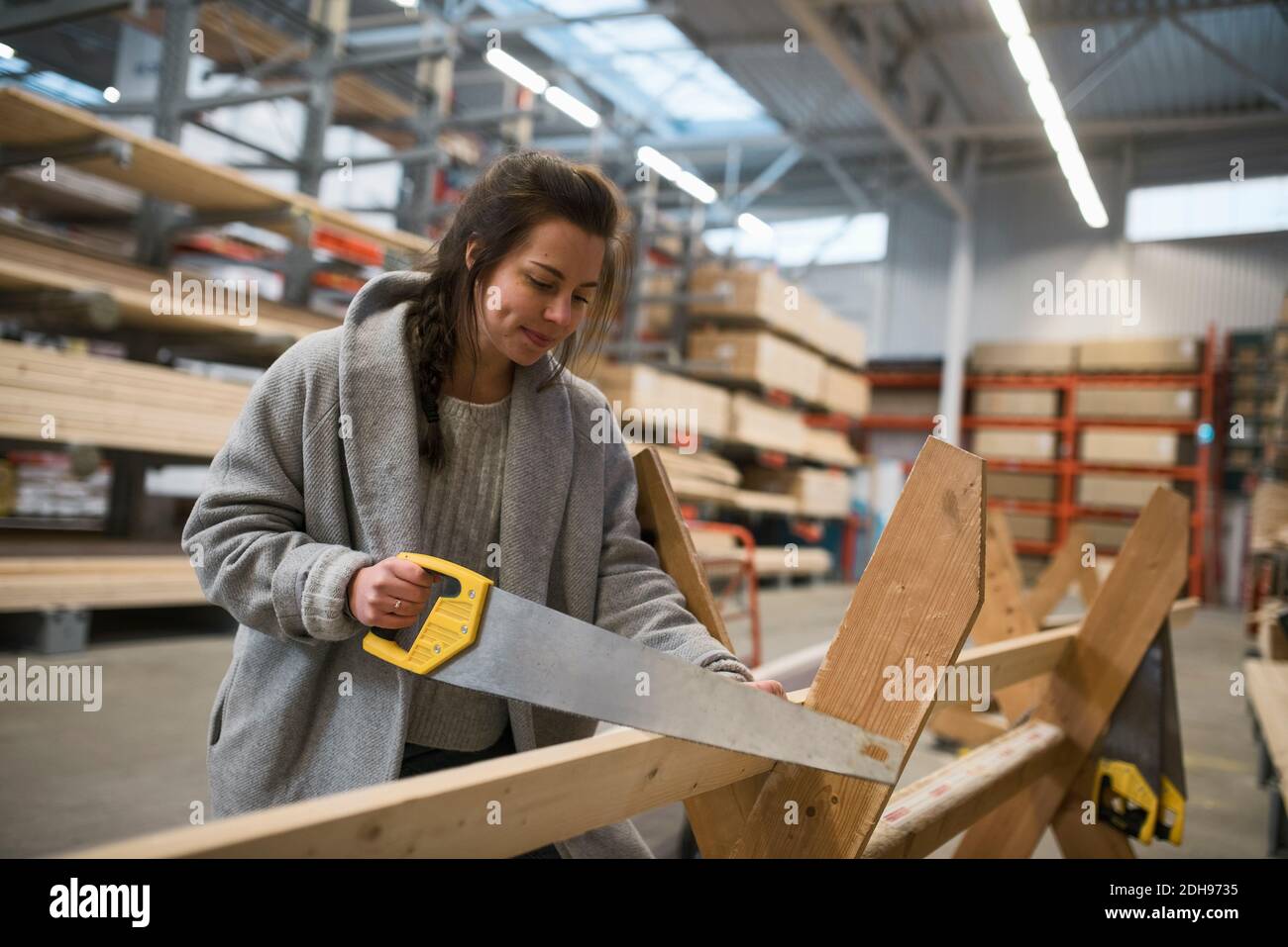 Client féminin coupant une planche en bois avec une scie à main dans un magasin de quincaillerie Banque D'Images