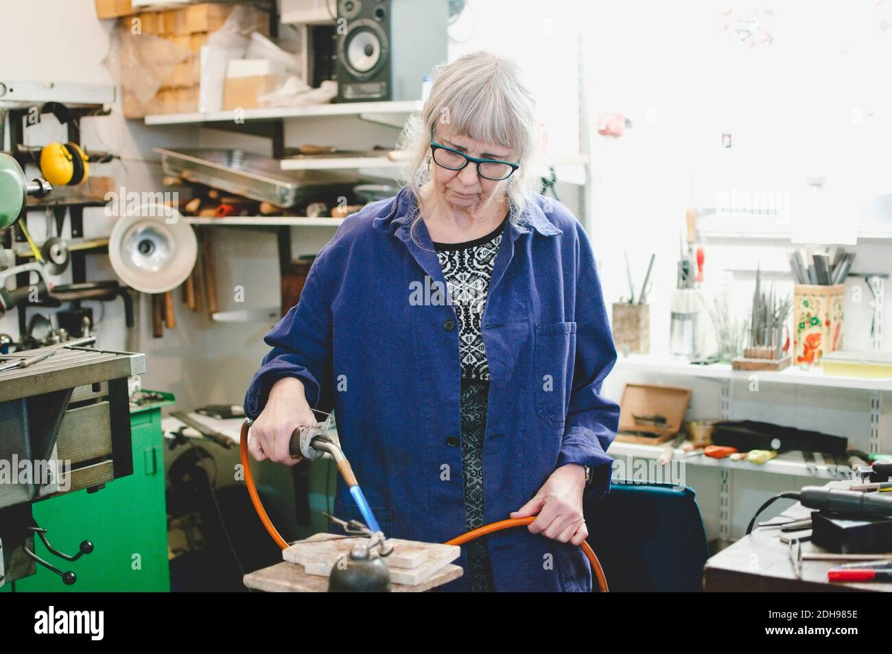 Artisan senior utilisant un chalumeau pour le travail des métaux dans un atelier de bijoux Banque D'Images