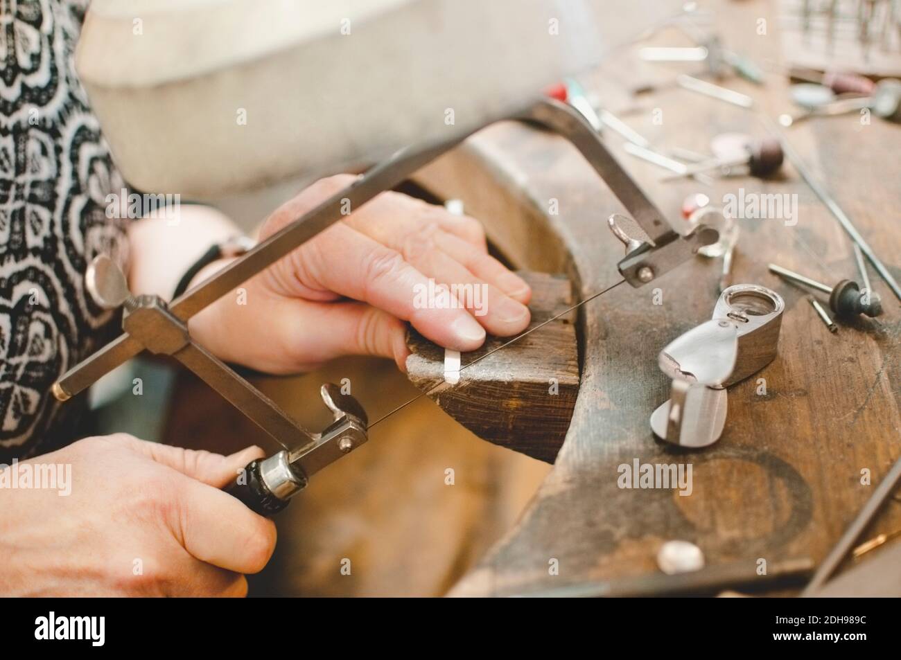 Image rognée d'une femme âgée coupant du métal avec une scie à main dans un atelier de bijoux Banque D'Images